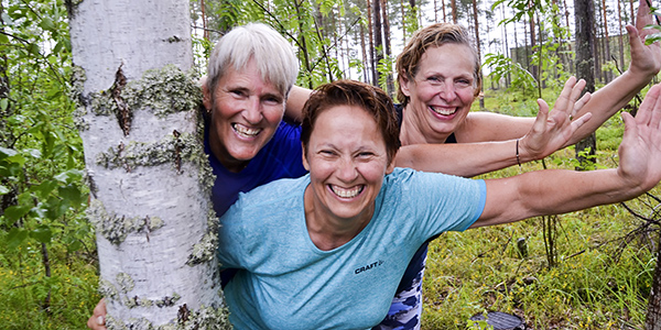 3 fornøyde damer smiler bredt her de står i skogen rundt et tre